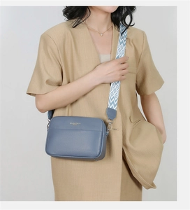 Detail of blue pebbled leather crossbody bag featuring geometric woven wide strap