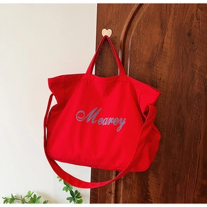 Détail du sac cabas en toile rouge avec lettrage Mearey suspendu à un crochet de porte
