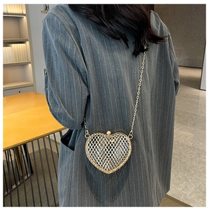 Detail of heart-shaped gold woven metal chain bag worn over a grey blazer
