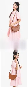 Brown moon-shaped leather saddle bag with adjustable strap shown on model's shoulder