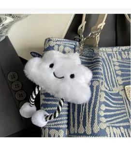 Detalle de un colgante de nube de felpa blanca con cara sonriente en un bolso de moda