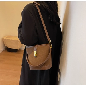 Brown vintage suede and leather bucket bag with gold buckle worn by a model in a coat