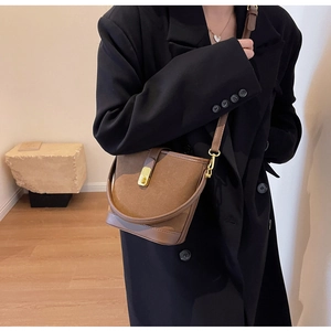 Detail of a brown suede bucket bag featuring golden metal clasp and adjustable leather strap