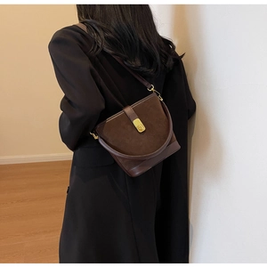 Close-up of deep brown crossbody bucket bag with gold clasp and suede-leather texture