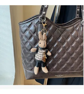 Close-up of brown quilted shoulder bag with fashion text and cute knit bunny pendant detail