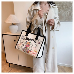 Detail of canvas tote bag featuring colorful graffiti teddy bear art and black handle straps