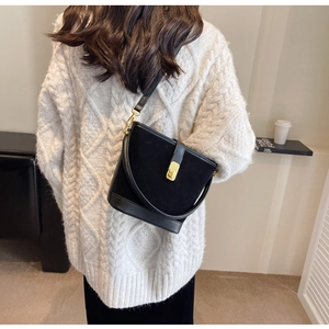 Detail of black crossbody bucket bag with gold lock and textured material contrast