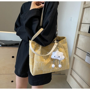 Detalle del bolso tote de lona amarilla con líneas geométricas y colgante de peluche