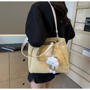 Detalle del bolso tote de jacquard amarillo con etiqueta de cuero blanco y colgante