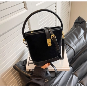 Detail of matte black bucket bag with gold clasp closure and glossy leather trim