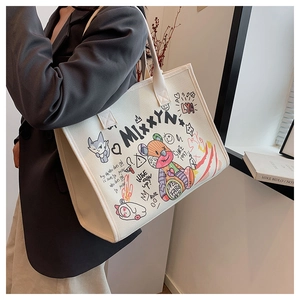 Model wearing a white canvas tote bag with artistic graffiti bear and cat illustrations