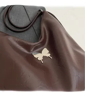 Detail of glossy dark brown faux leather bag with polished gold butterfly buckle