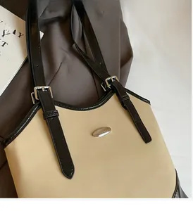 Close-up of silver logo plate and adjustable buckle on a beige leather tote bag