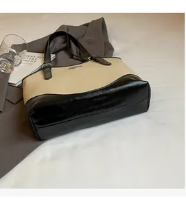 Detail of beige and black contrast shoulder bag with oval metal logo on a stylish desk