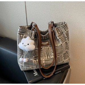 Detalle de bolso tote de tela con rayas geométricas, asas de cuero y colgante de nube