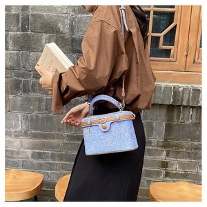 Detail of blue denim bucket bag with brown leather trim held by model outdoors