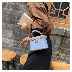 Detail of blue denim barrel bag with brown leather trim and metal clasp in a garden setting