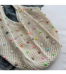 Detail of hand-woven beige knit bag featuring colorful imitation pearls and wide shoulder strap
