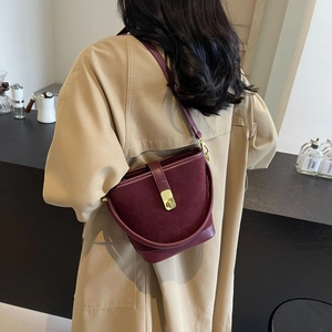 Burgundy bucket shoulder bag in mixed leather finish with gold clasp on beige coat