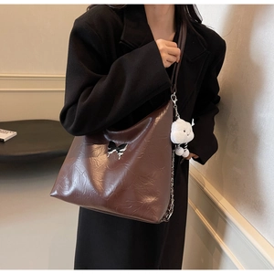 Detail view of brown leather hobo bag with bow charm and cute plush toy hanging accessory