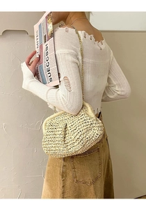 Detail of a beige woven straw cloud bag with a delicate gold metal chain strap on a model