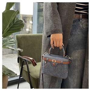 Close-up of vintage denim box bag with leather handle and pocket detail on green chair