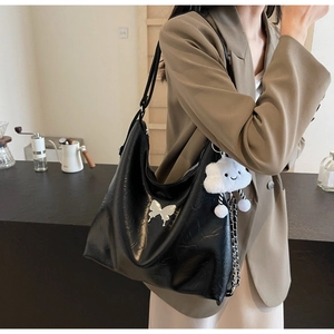 Detail of black faux leather tote bag with silver butterfly charm and plush white cloud pendant