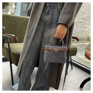 Detail of blue denim box bag with brown leather trim and retro pocket design