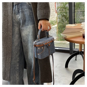 Detail of vintage denim box bag with brown leather trim and metal rivets in a lifestyle setting