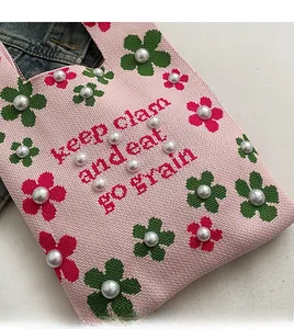 Close-up of pink knit bucket bag with floral patterns, pearls, and lettered texture
