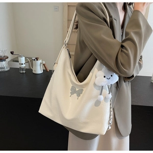 Detail of off-white tote bag with silver butterfly charm and plush cloud accessory