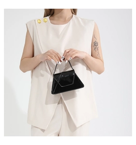 Detail of elegant black patent leather shoulder bag with triangle shape held by a model