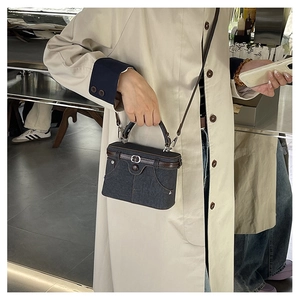 Outdoor street style shot of a dark blue denim crossbody bag with brown leather details