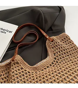 Close-up of woven straw tote bag featuring brown leather straps and gold rivets