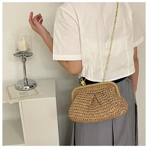 Detail of a beige woven straw cloud bag with a slim gold metal chain shoulder strap