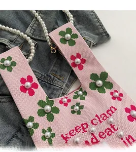 Detail view of pink knitted bucket bag with floral patterns and white pearl embellishments