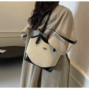 Detail view of beige and black contrast tote bag worn by a model in a minimalist setting