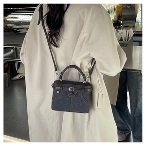Detail view of denim handbag with leather trim and gold metal lock on a female model