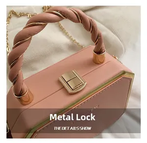 Detail of pink geometric box bag showing gold twist lock and designer braided handle