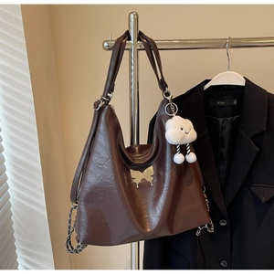 Detail of dark brown leather tote with gold butterfly logo and plush cloud charm