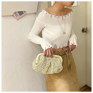 Detail of a chic beige straw clutch bag styled with a white off-shoulder knit top
