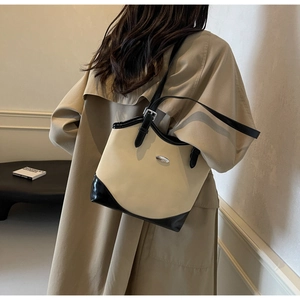 Detail of minimalist beige and black leather tote bag featuring elegant metal logo plate