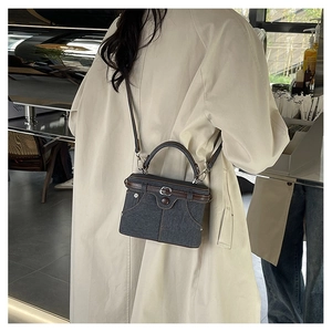 Close-up of a retro denim and leather crossbody bag styled with a beige coat in a cafe