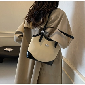 Detail of beige and black tote bag showing metal logo and adjustable shoulder straps