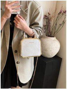 Detail of white octagonal box bag featuring gold metal frame and twisted handle