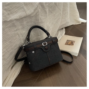 Detail of dark blue denim crossbody bag featuring brown leather trim and pocket design