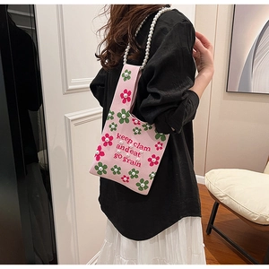 Close-up of pink knitted bucket bag with floral embroidery and pearl chain handle