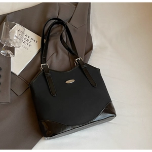 Detail of black tote bag with silver logo plate on professional brown suit backdrop