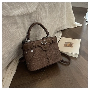 Detail of a brown denim textured handbag with metal rivets on dark wood flooring