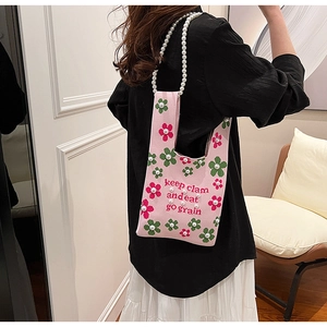 Detail of pink knitted bucket bag featuring floral patterns and a pearl handle strap
